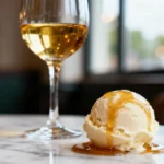 Gros plan d'une boule de glace à la vanille nappée de miel avec un verre de sauternes doré sur table en marbre