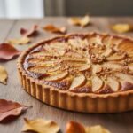 Tarte française Bourdaloue avec amandes caramélisées et tranches de poires disposées en éventail sur fond de table en bois