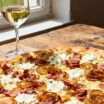 Tarte flambée croustillante aux oignons caramélisés et lardons, accompagnée d'un verre de riesling d'Alsace sur table en bois